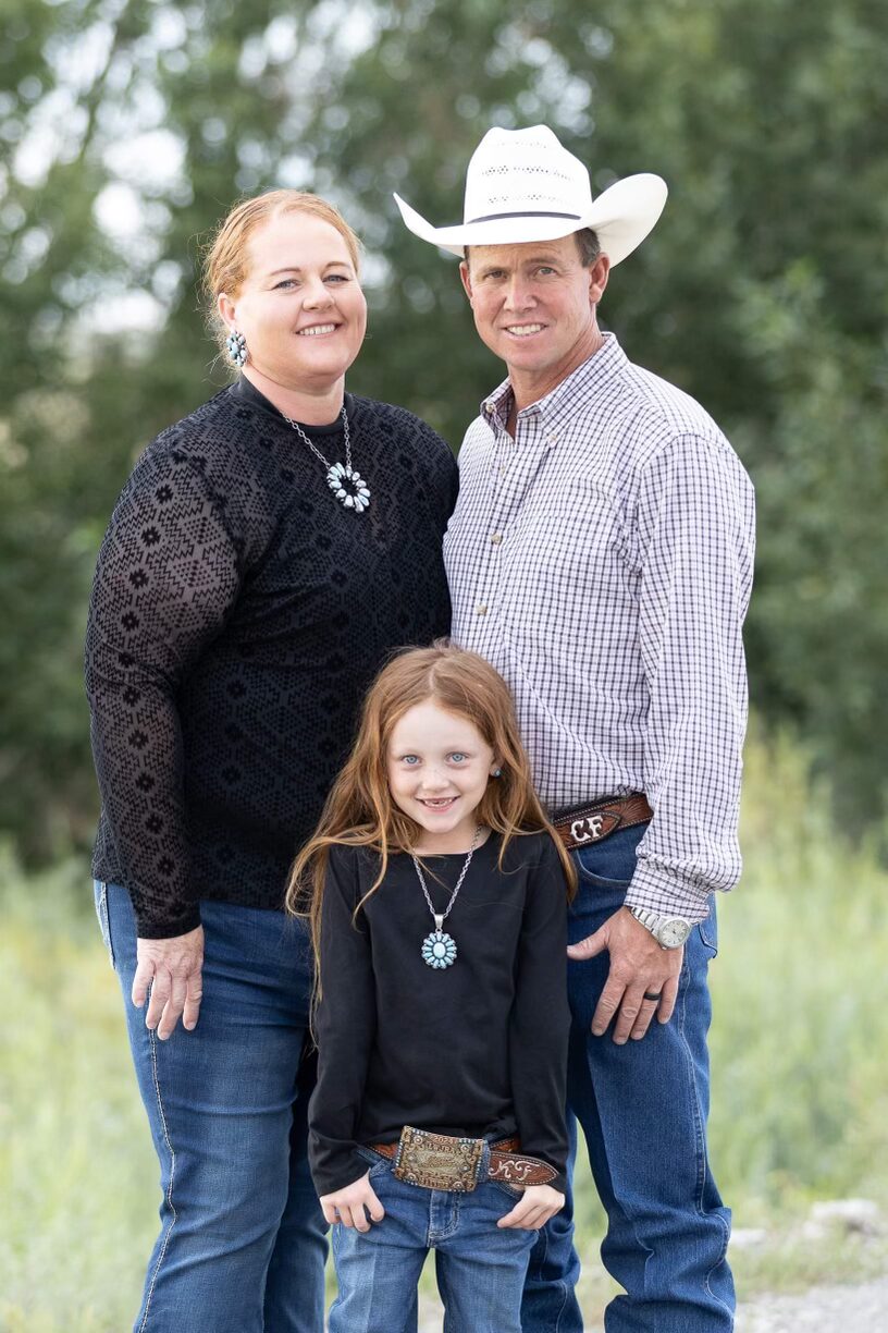 Family of three wearing Western attire and jewelry posing outdoors with trees in background