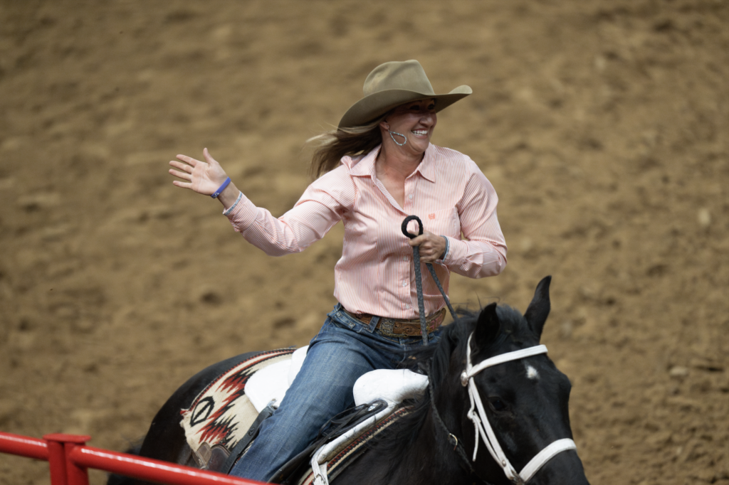 Barrel racer in pink shirt and cowboy hat guides her black and white horse around a red barrel during competition