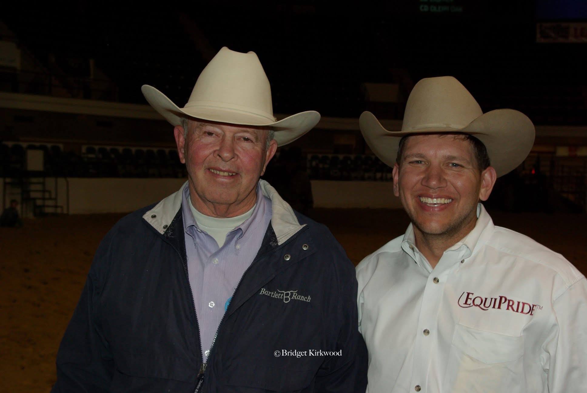Two smiling men in cowboy hats pose side by side in an arena, one in a Bartlett Ranch jacket and one in an EquiPride shirt