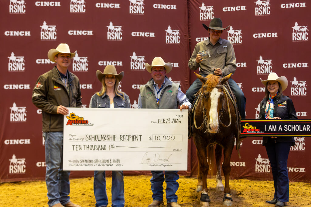 Four people in cowboy hats hold an oversized $10,000 San Antonio Stock Show & Rodeo scholarship check beside a mounted rider on a sorrel horse