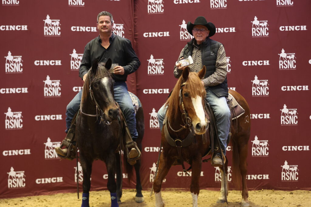 Two mounted riders pose with awards in front of a maroon Cinch RSNC backdrop after a ranch sorting competition