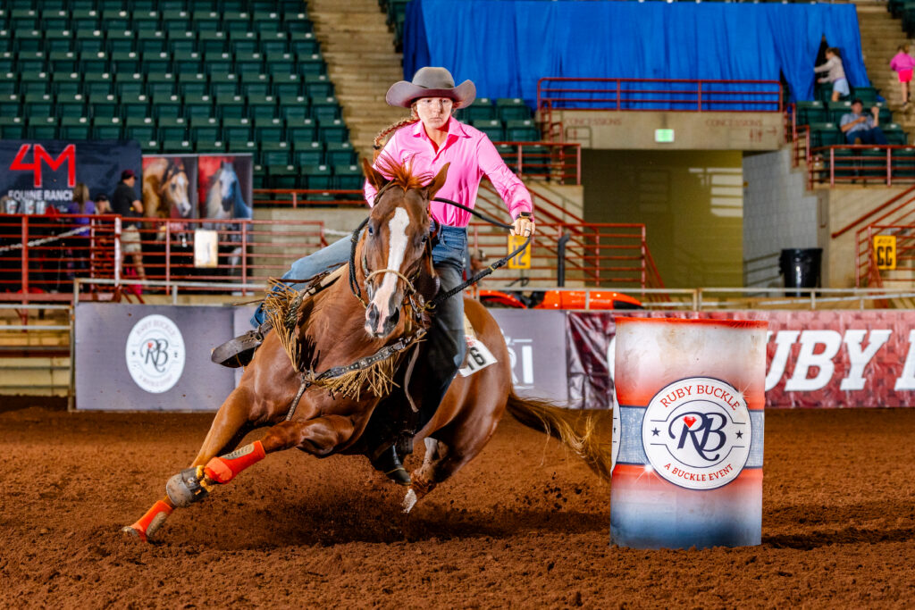 person in a pink shirt turns a barrel on a red horse