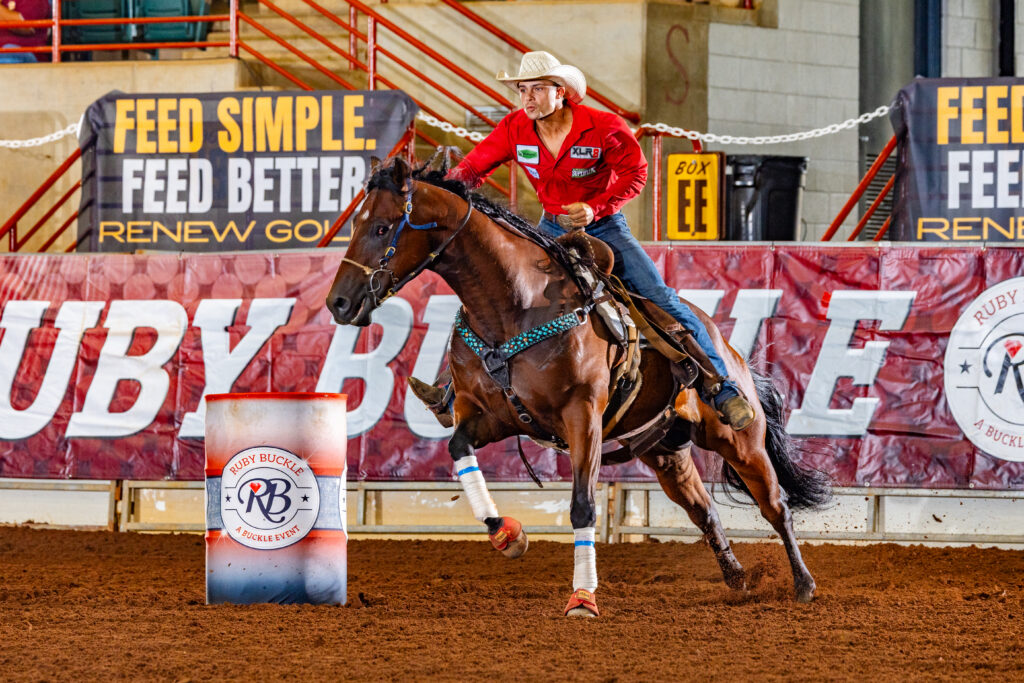 A man in a red shirt turns a barrel on a horse