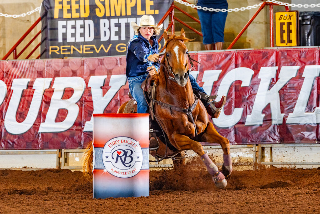 A girl in a blue shirt turns a barrel on a red horse 