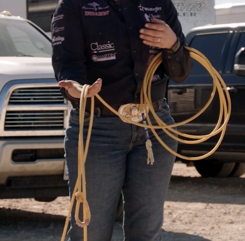 Roper in a sponsor-patched shirt and trophy buckle holds a coiled nylon rope with the honda loop resting in one hand