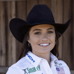 Smiling young woman in a black cowboy hat and white sponsor-patched shirt wearing a rodeo queen sash outdoors