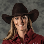 Smiling rodeo competitor in a dark brown cowboy hat and maroon western shirt poses for a headshot against a gray backdrop