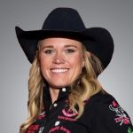 Smiling blonde woman in a black cowboy hat and black embroidered western shirt posing for a headshot against a gray backdrop