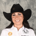 Smiling young woman in a black cowboy hat and white embroidered western shirt posing for a headshot against a gray backdrop