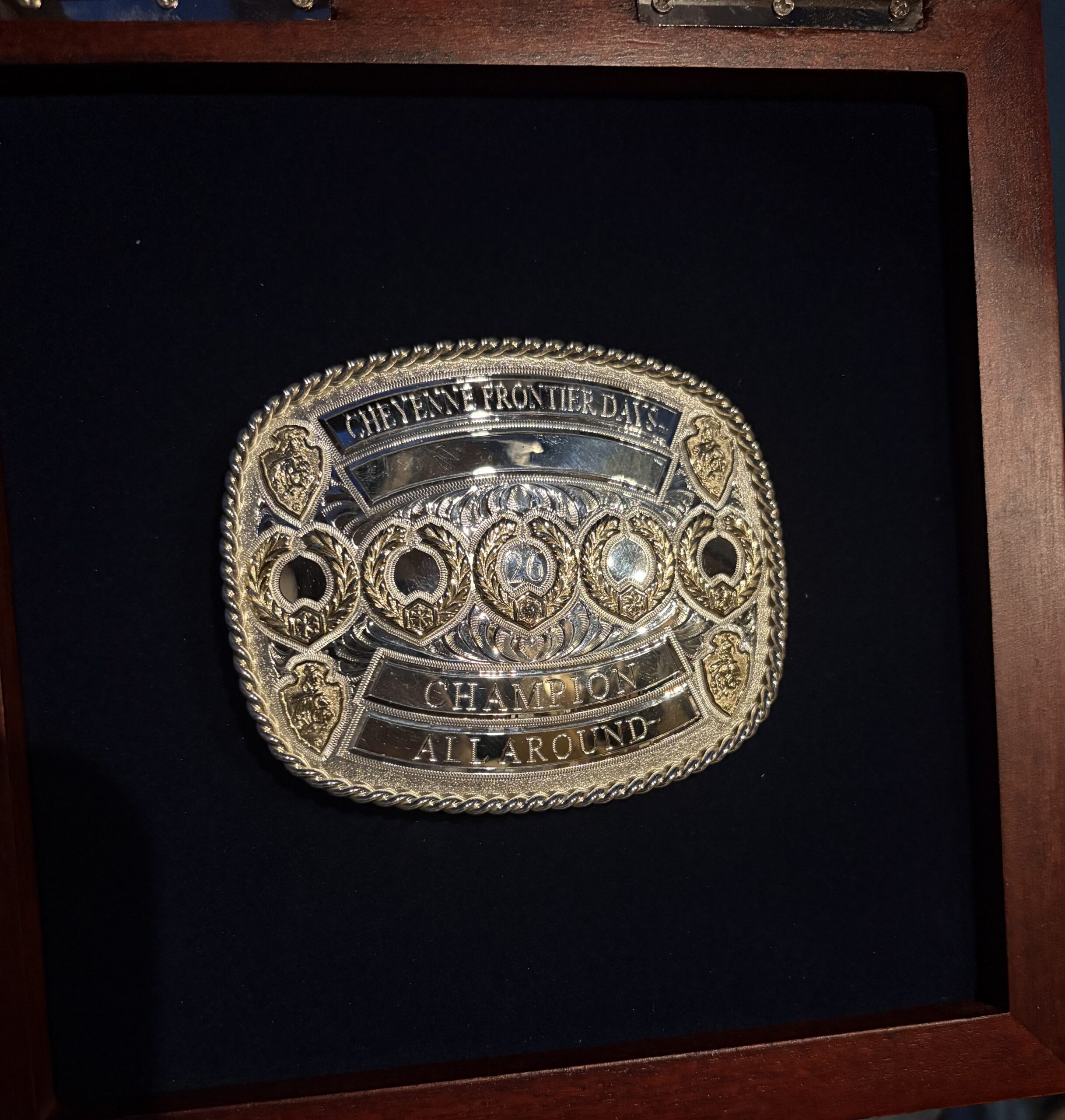 Cheyenne Frontier Days Champion All Around ornate belt buckle displayed on dark blue fabric in wooden case
