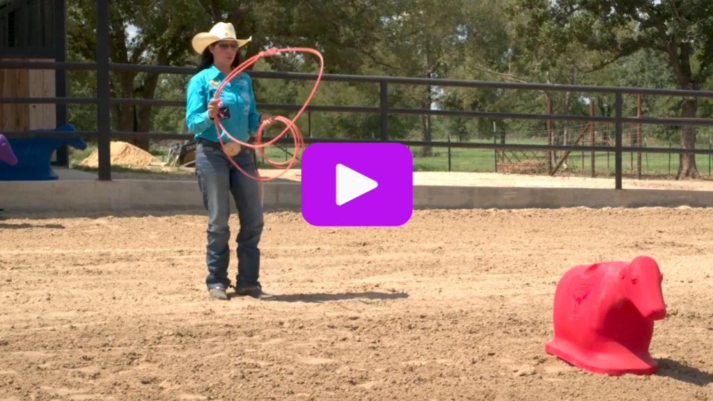 Roper in a straw cowboy hat and turquoise shirt swings a loop toward a red roping dummy in a sandy arena