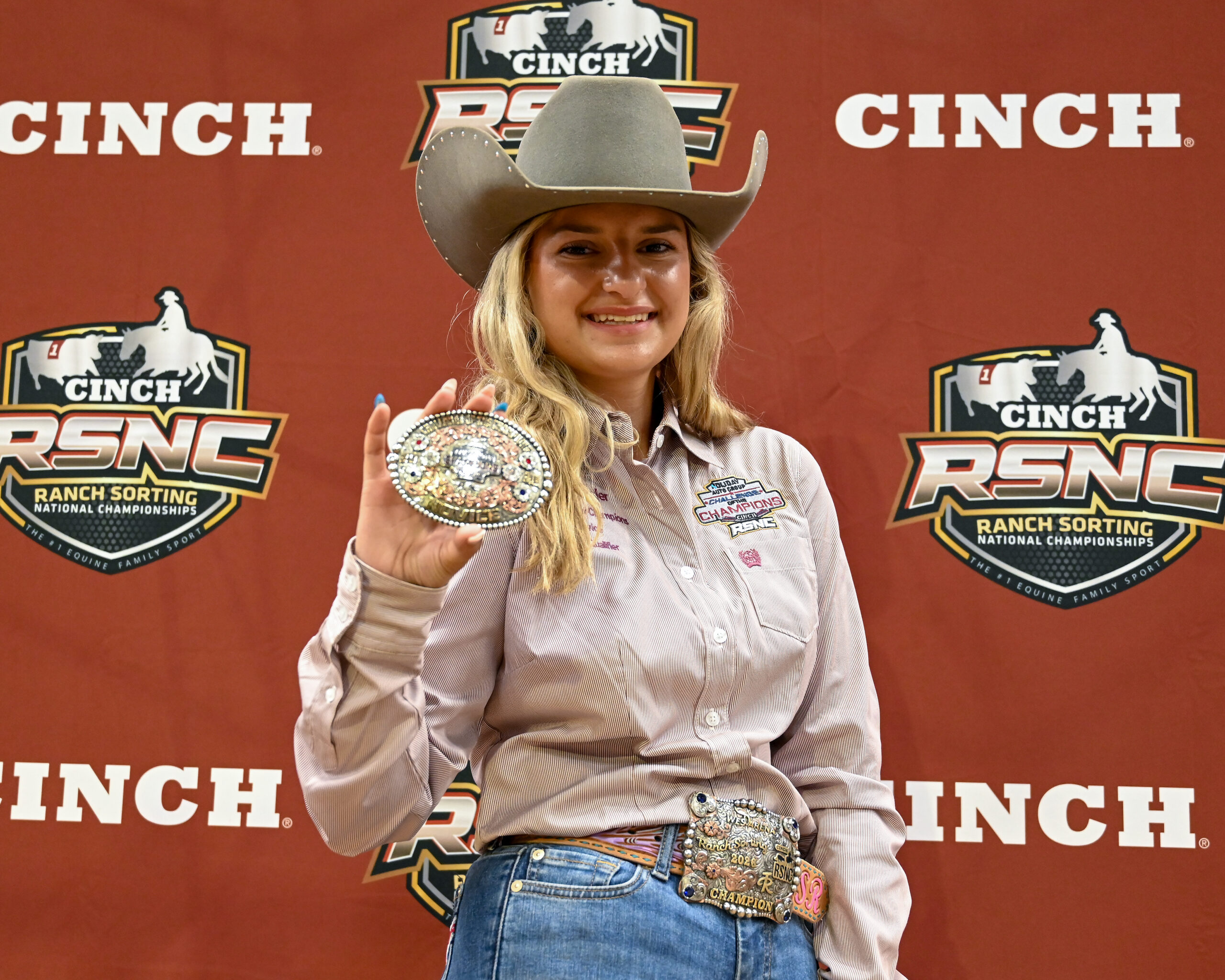 Champion posing with buckle and belt at Cinch RSNC Ranch Sorting National Championships backdrop