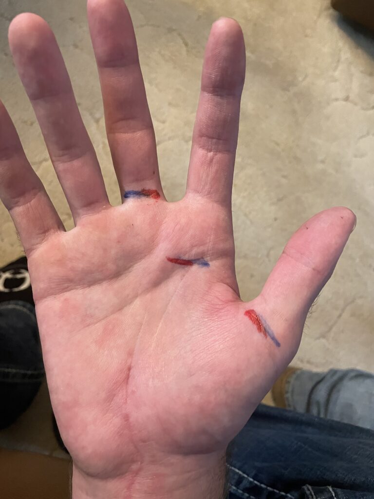 Open palm marked with three short red and blue pen lines showing rope placement points across the fingers and hand