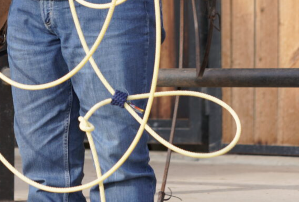 Close-up of a roper in blue jeans holding a coiled nylon lariat with a burner-wrapped honda loop at his side