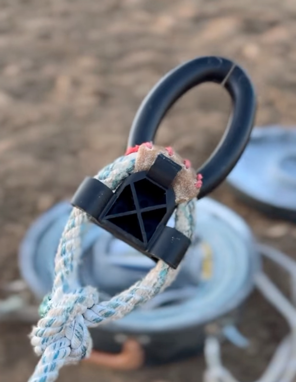 Close-up of a rope halter's black plastic fiador knot block and O-ring, with a coiled rope in the background