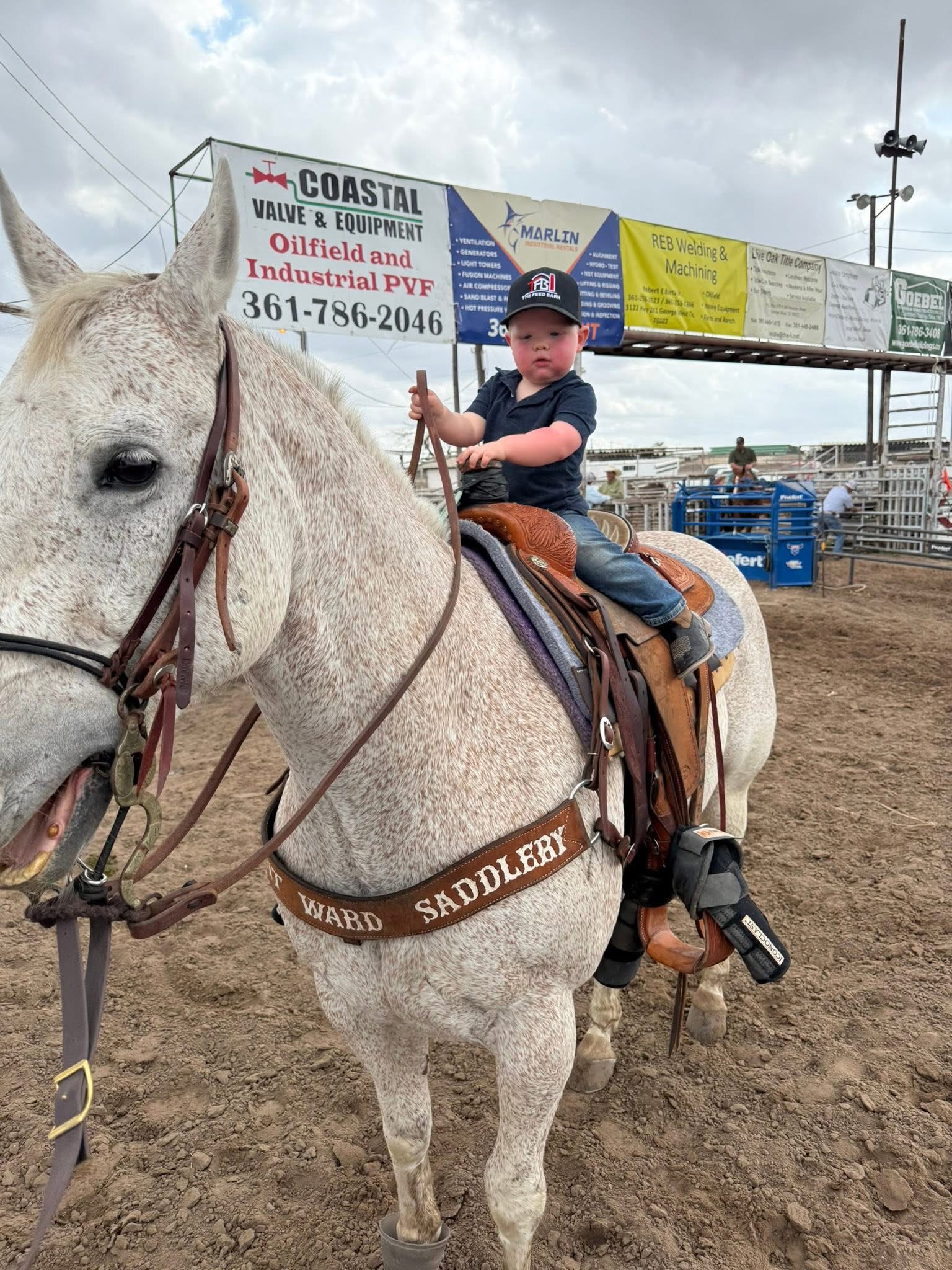 Young rider on gray horse with "Ward Saddlery" saddle at rodeo arena during daytime event