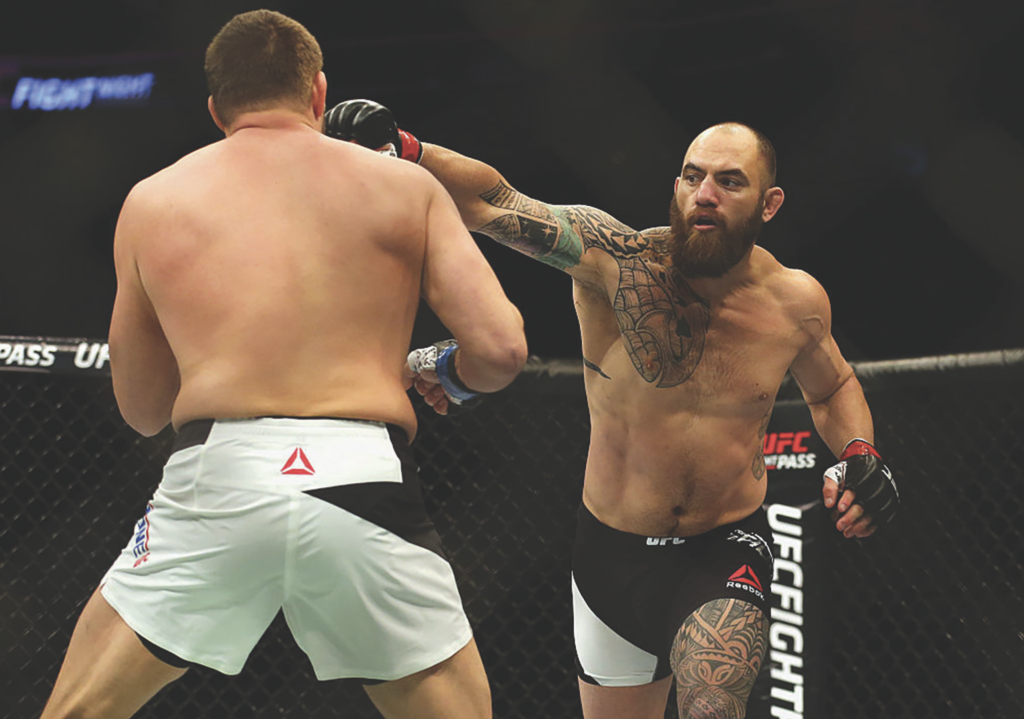 Bearded tattooed MMA fighter lands a straight left punch to his opponent's guard inside the cage