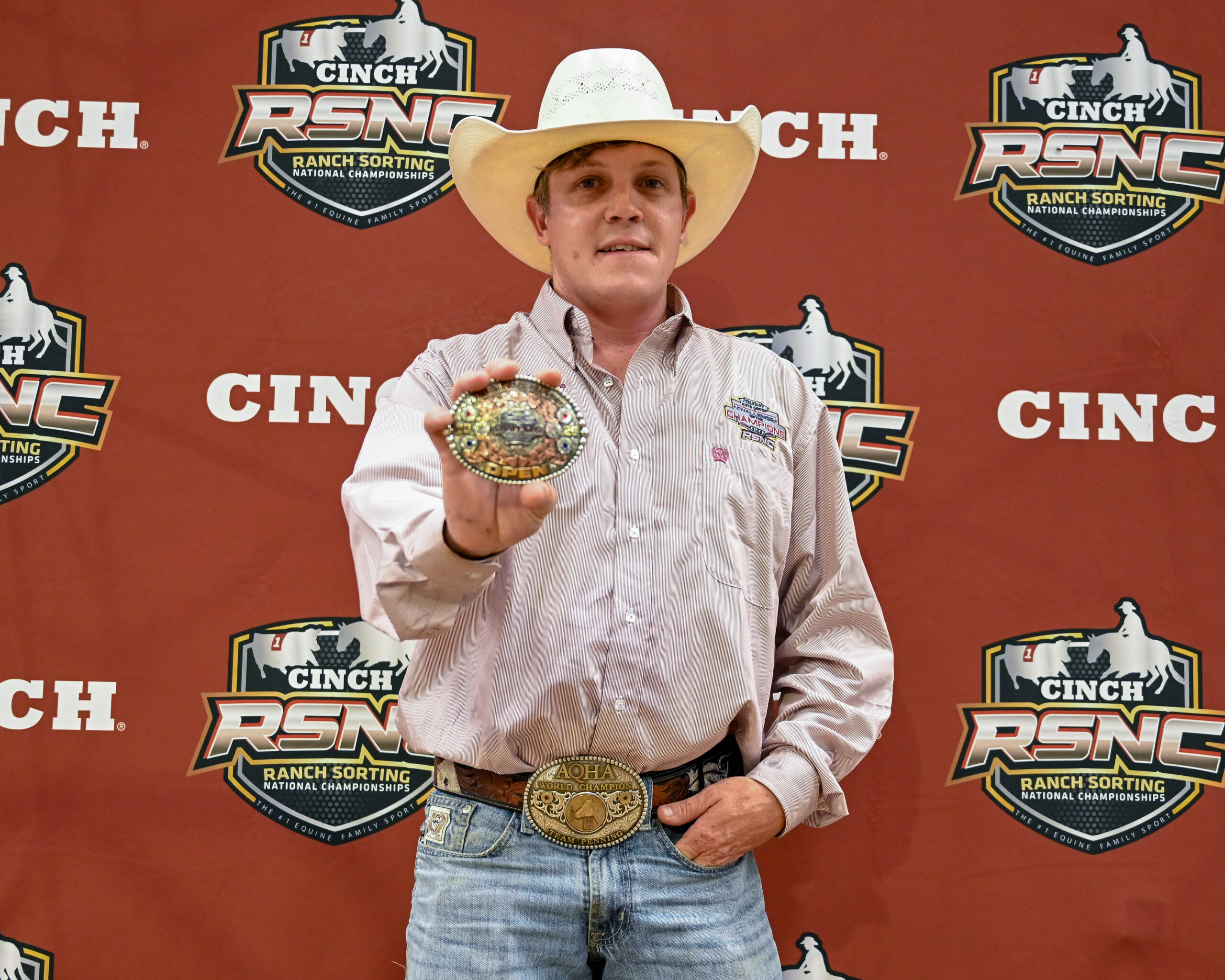 Cowboy holding ornate belt buckle and trophy at Cinch RSNC Ranch Sorting National Championships backdrop