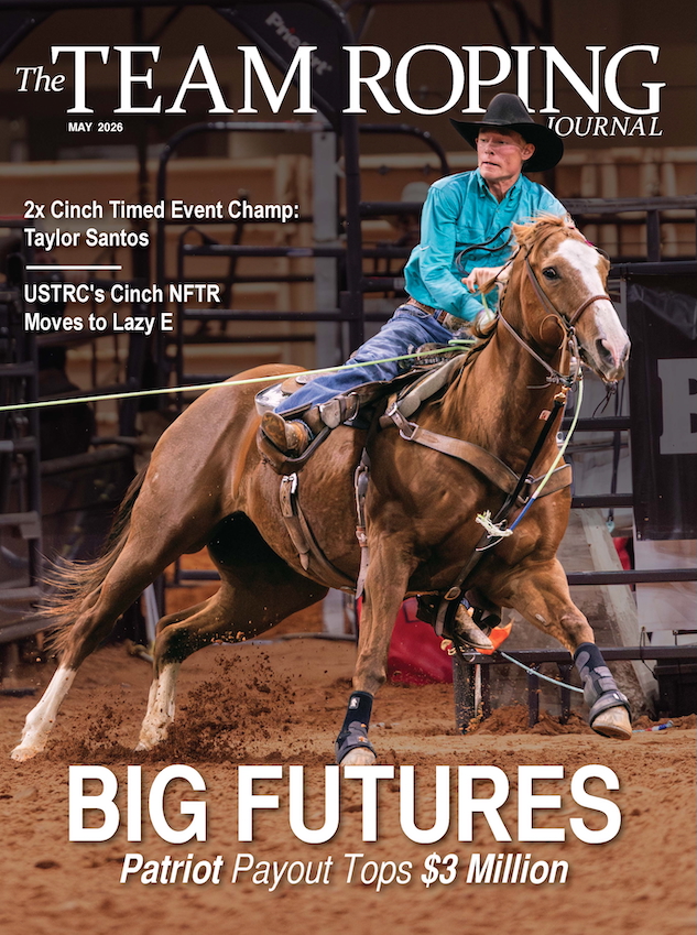 Cowboy in turquoise shirt and black hat on brown horse competing in team roping event in indoor arena