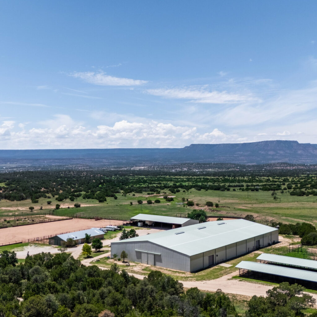 Modern equestrian facility with large arena buildings and roping pens on sprawling Colorado ranch beneath flat-topped mountain