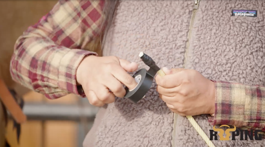Close-up of a roper wrapping black tape around the end of a team roping rope with a roll of electrical tape