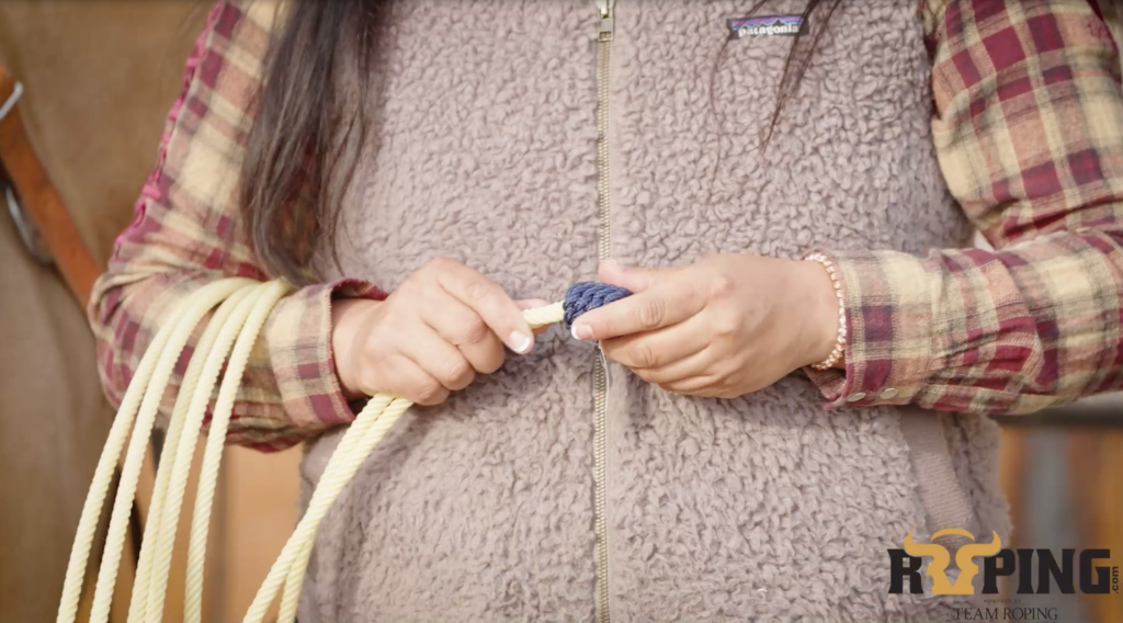 Close-up of a roper's hands adjusting the blue burner and honda knot on a coiled team roping rope