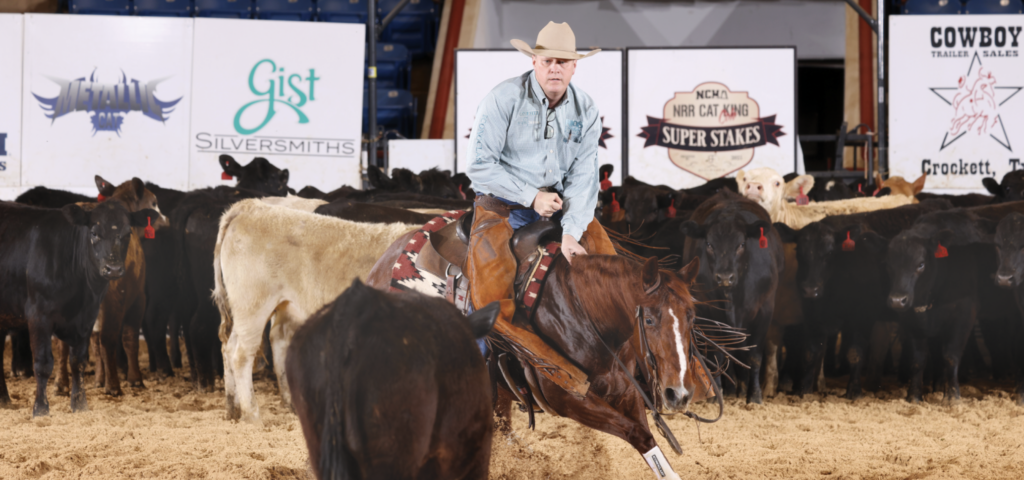 Cowboy on horseback roping cattle in an arena with spectators and sponsor banners in the background