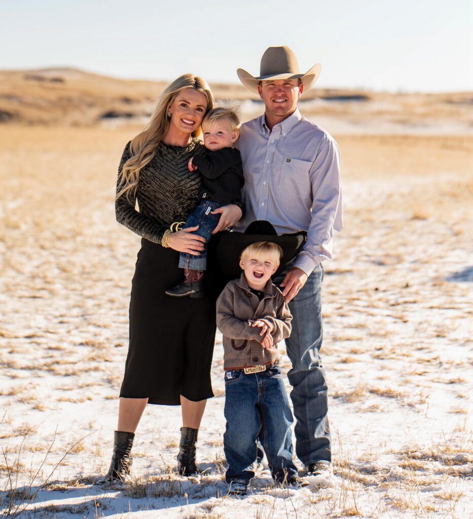 Family of four in Western attire, including a cowboy hat, posing together in a snow-dusted prairie pasture