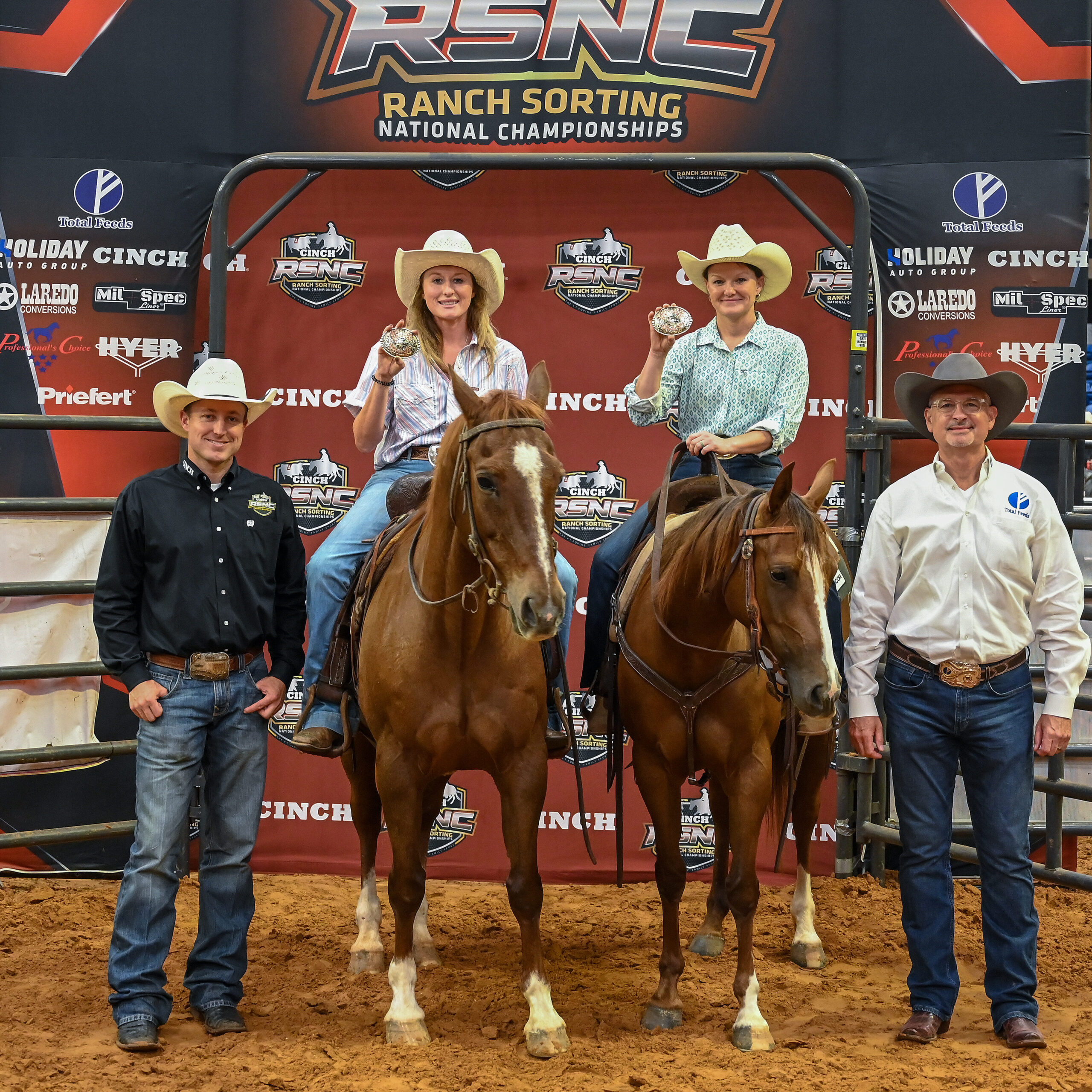 Two women on horseback hold up championship buckles beside two men standing in the arena dirt at an RSNC ranch sorting backdrop