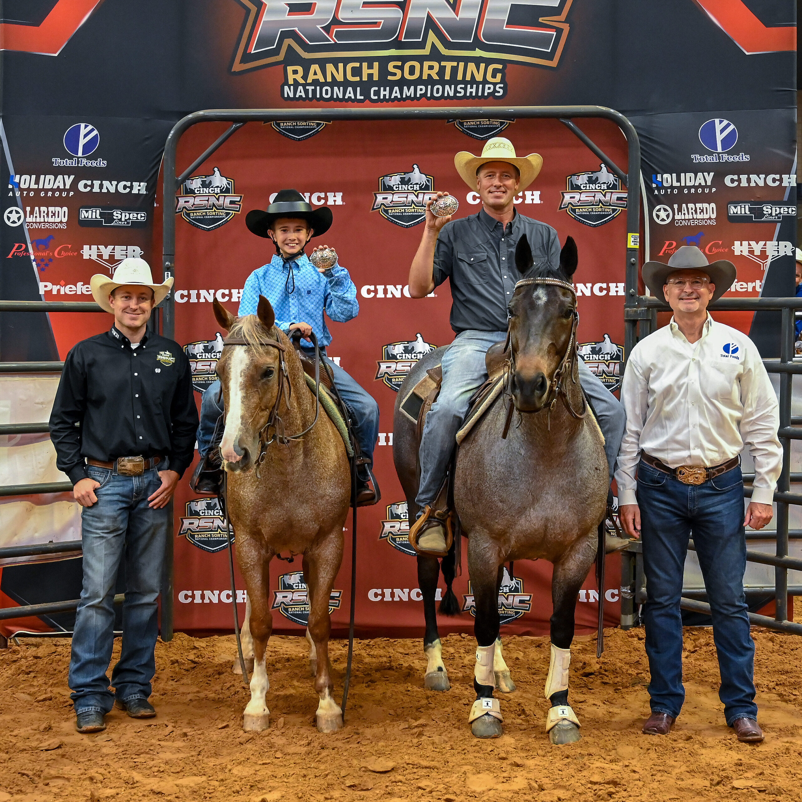 Young rider and adult partner hold up championship buckles from horseback beside two men at a Cinch RSNC ranch sorting backdrop
