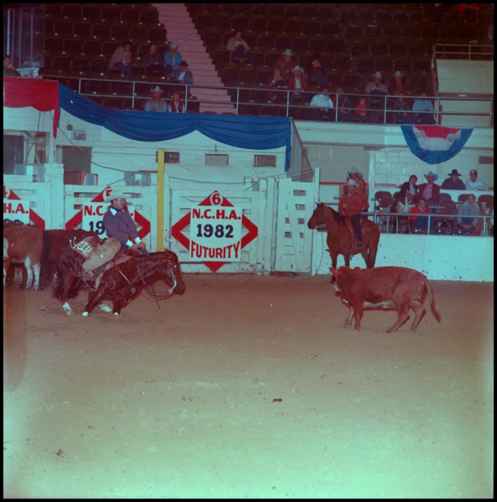 Cutting horse and rider work a cow in the arena as a turnback rider waits, with NCHA 1982 Futurity signage behind them