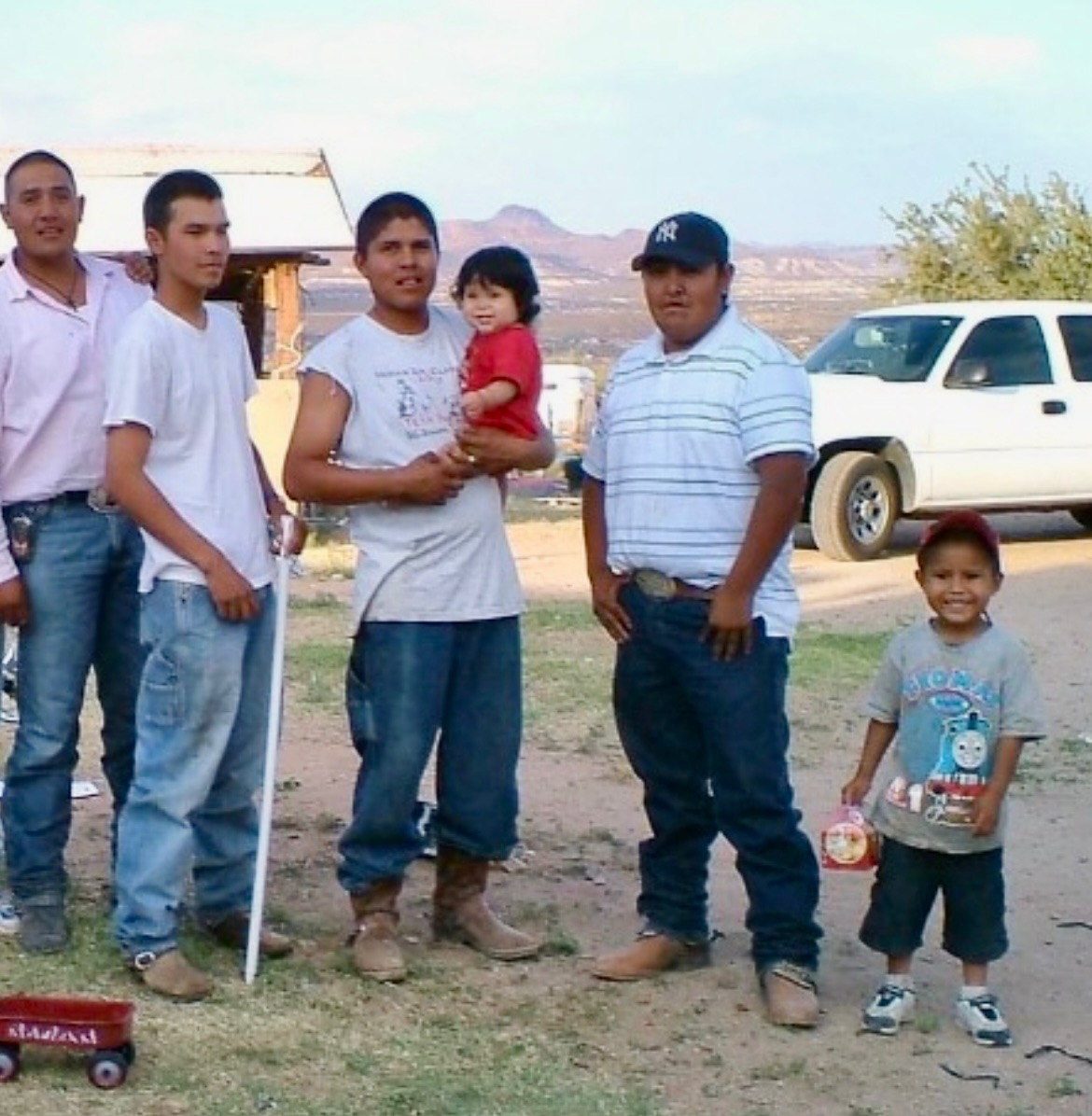 Family group posing outdoors with mountains in background and white pickup truck nearby