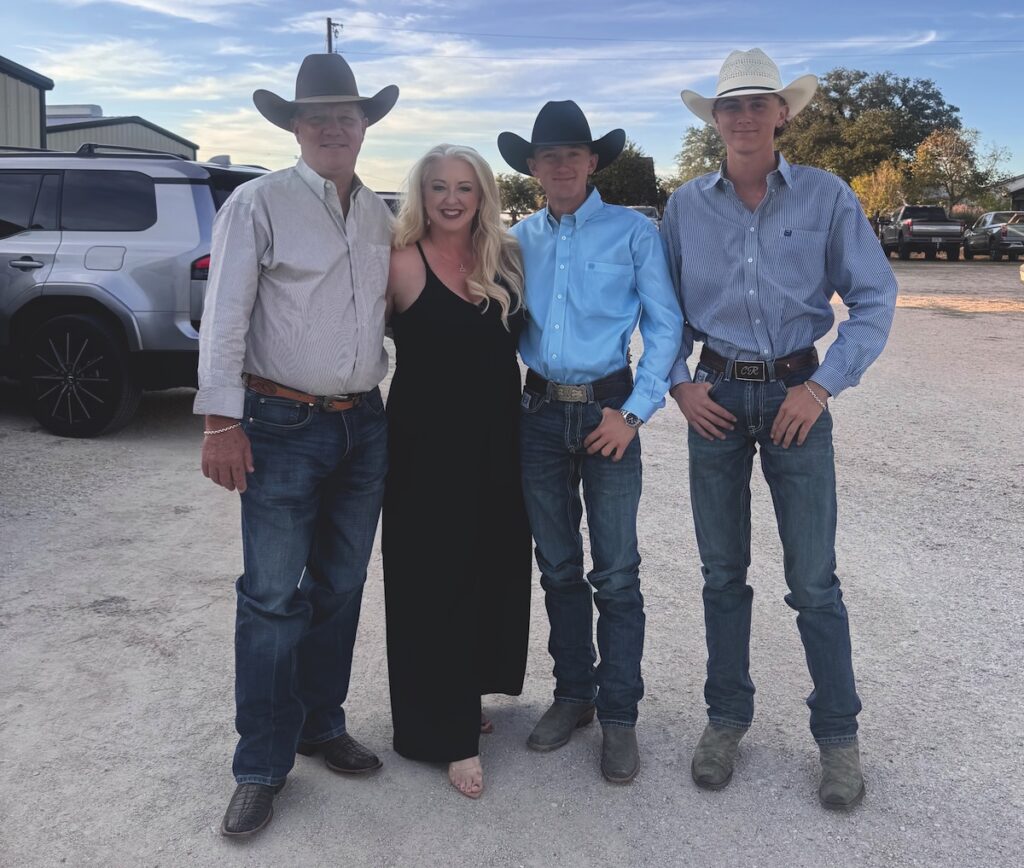 Family of four in cowboy hats, jeans and boots poses together on a gravel lot at a rodeo event