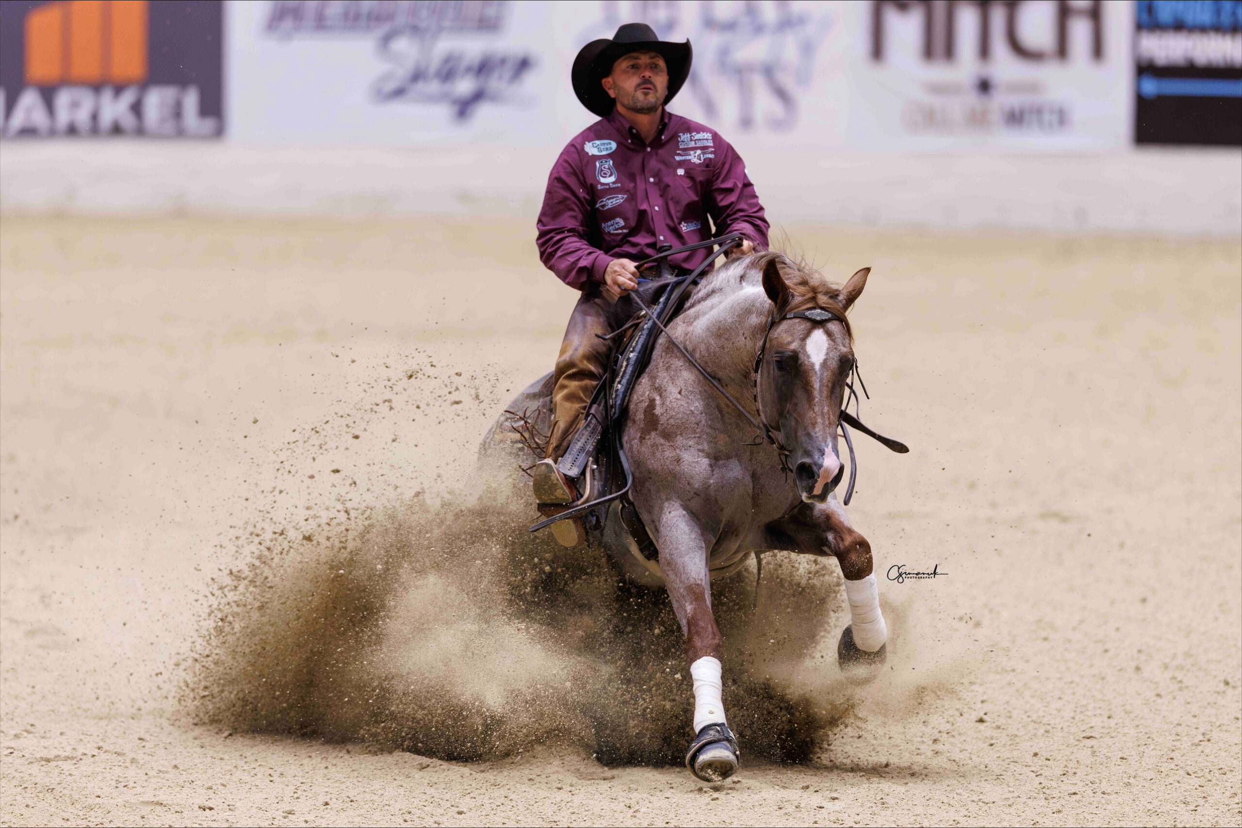 Barrel racer in purple shirt rounds a barrel on a sorrel horse, kicking up dust in the arena