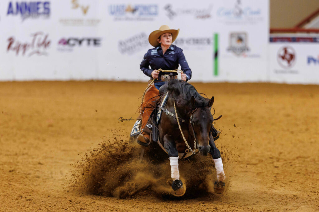Reiner in a straw cowboy hat slides her bay horse to a stop, kicking up a spray of arena dirt