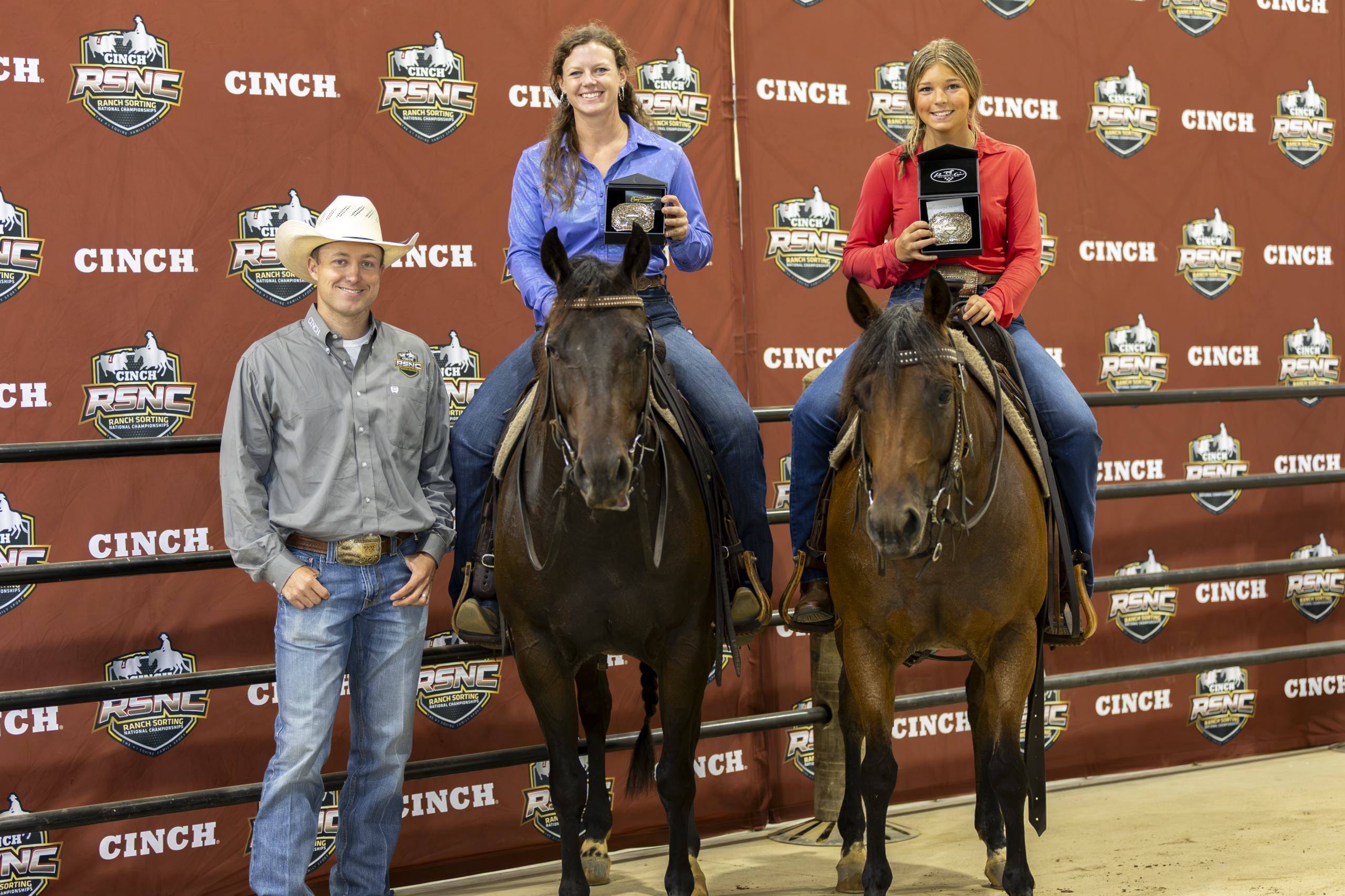 Barrel racing winners pose with their horses at a CINCH-sponsored event, with a man standing beside them against a branded backdrop