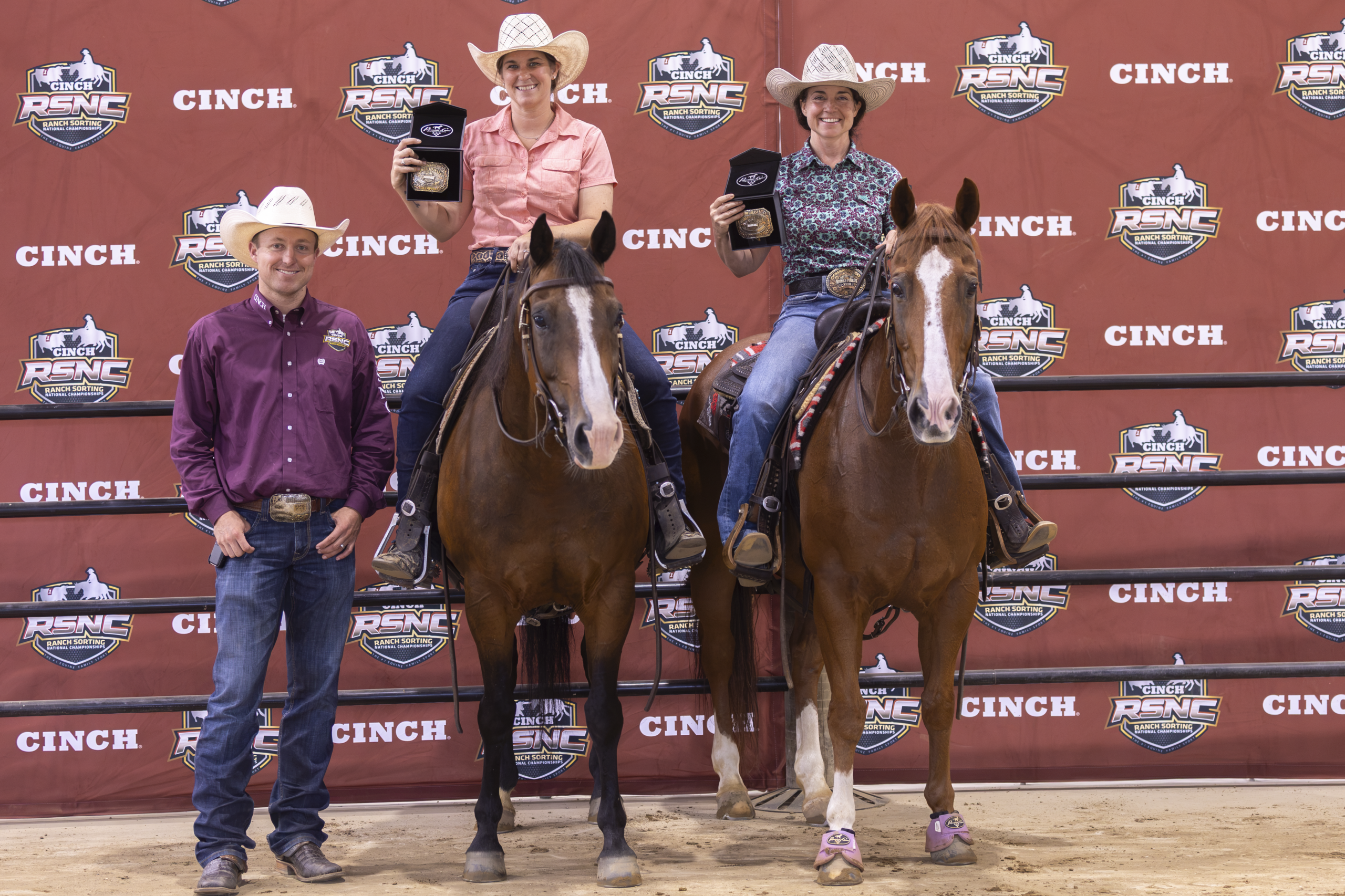 Three riders on horseback pose with a handler at a Cinch RSNC event backdrop during an awards presentation