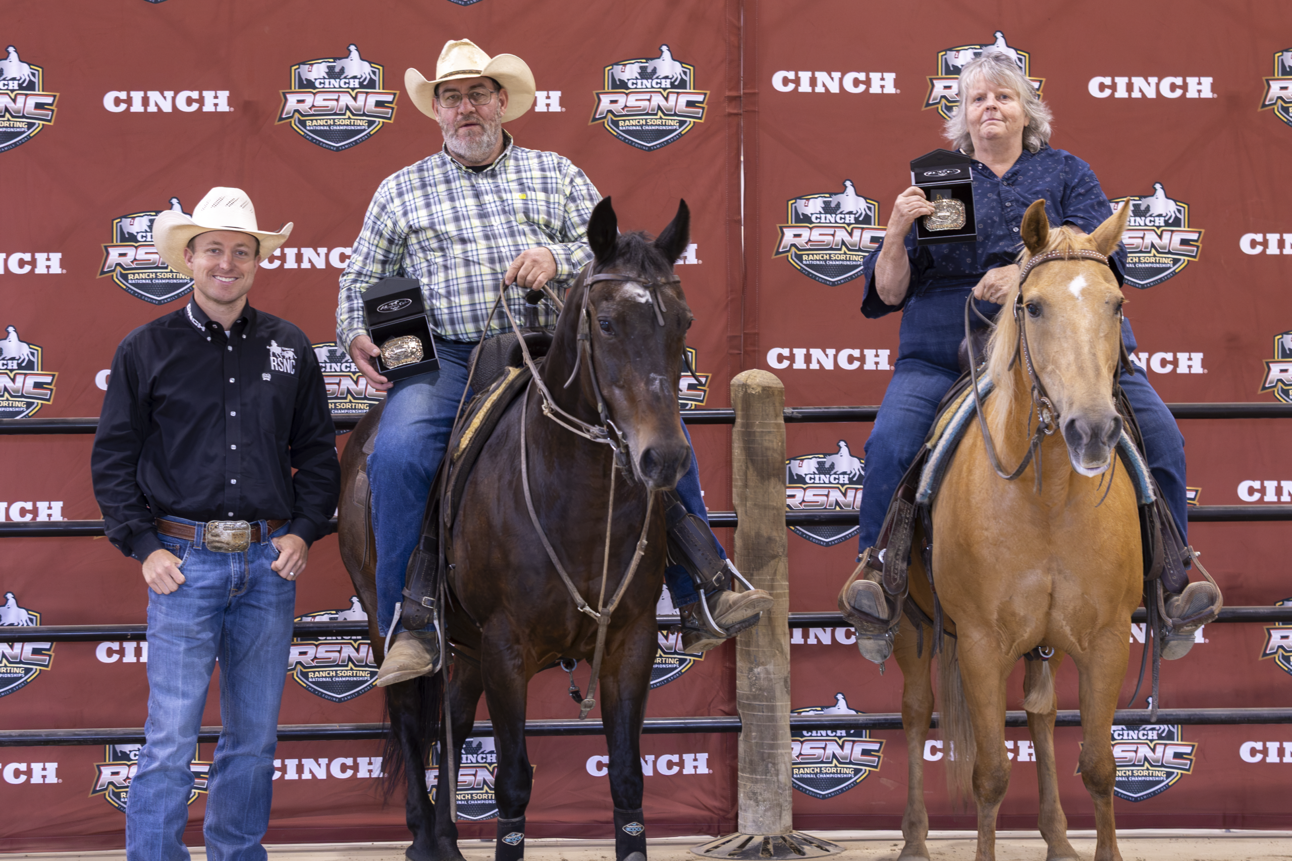 Three cowboys on horses stand before a Cinch-branded backdrop at a rodeo event