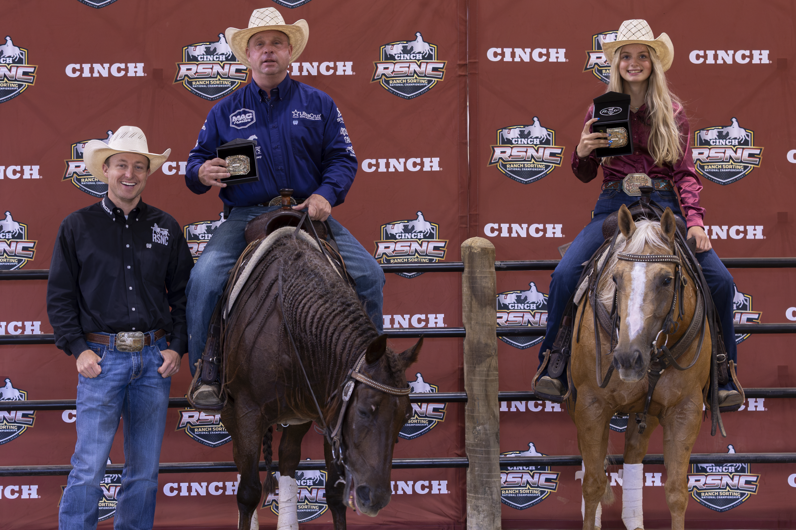 Cowboys and cowgirls pose with horses in front of Cinch branded backdrop at rodeo event
