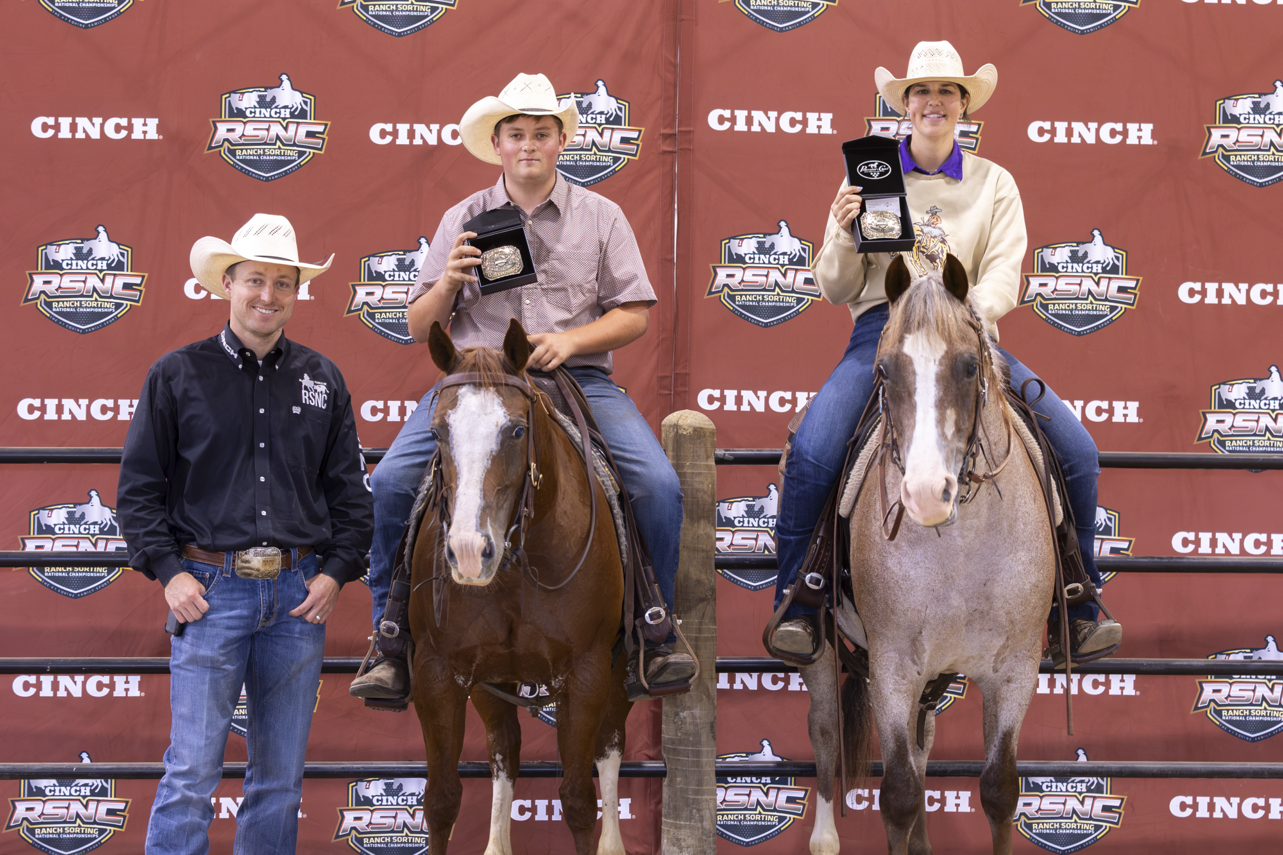 Three cowboys stand with their horses at a Cinch RSNC podium during an awards presentation