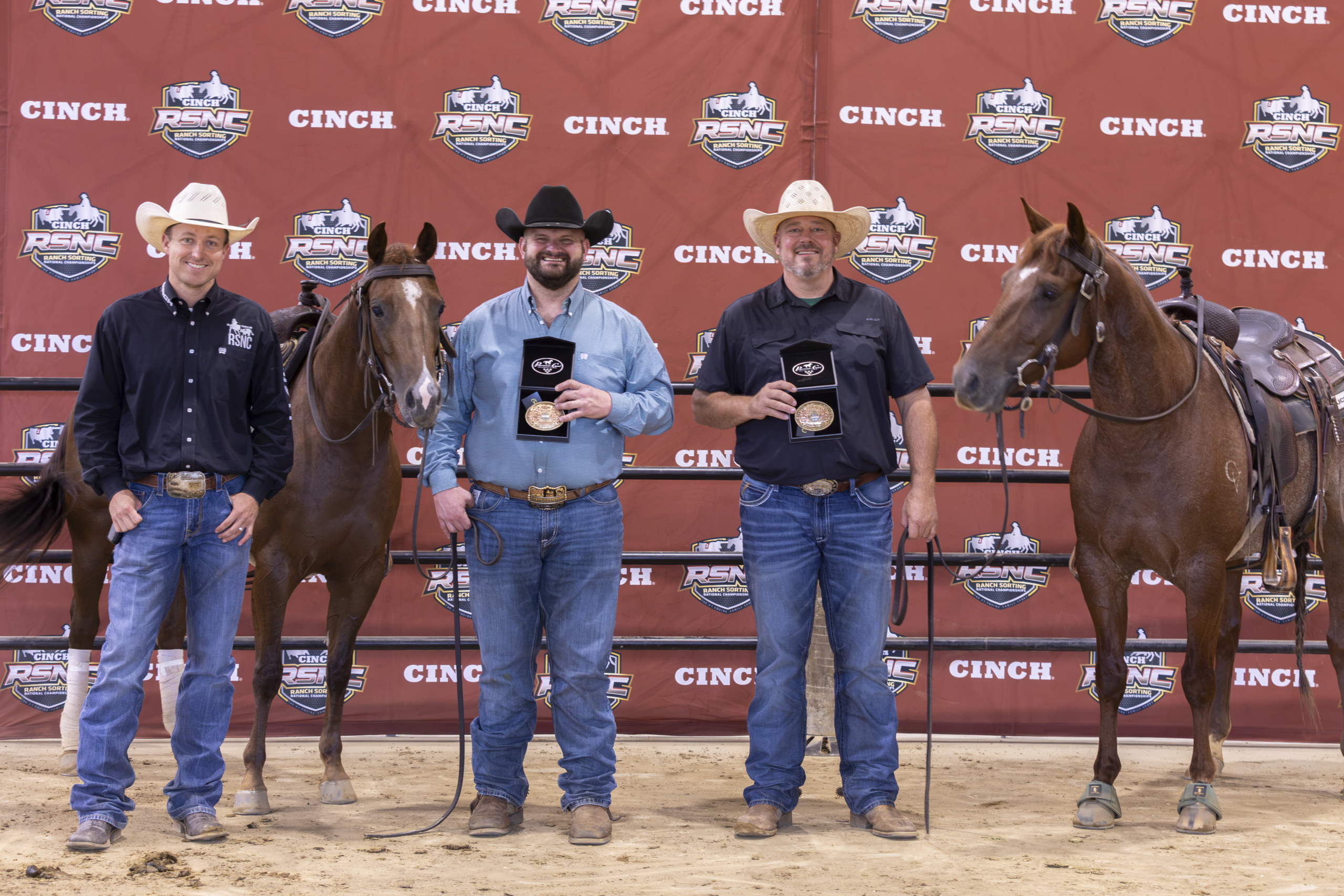 Five cowboys and two horses stand at a CINCH-branded backdrop during an awards presentation at a rodeo event