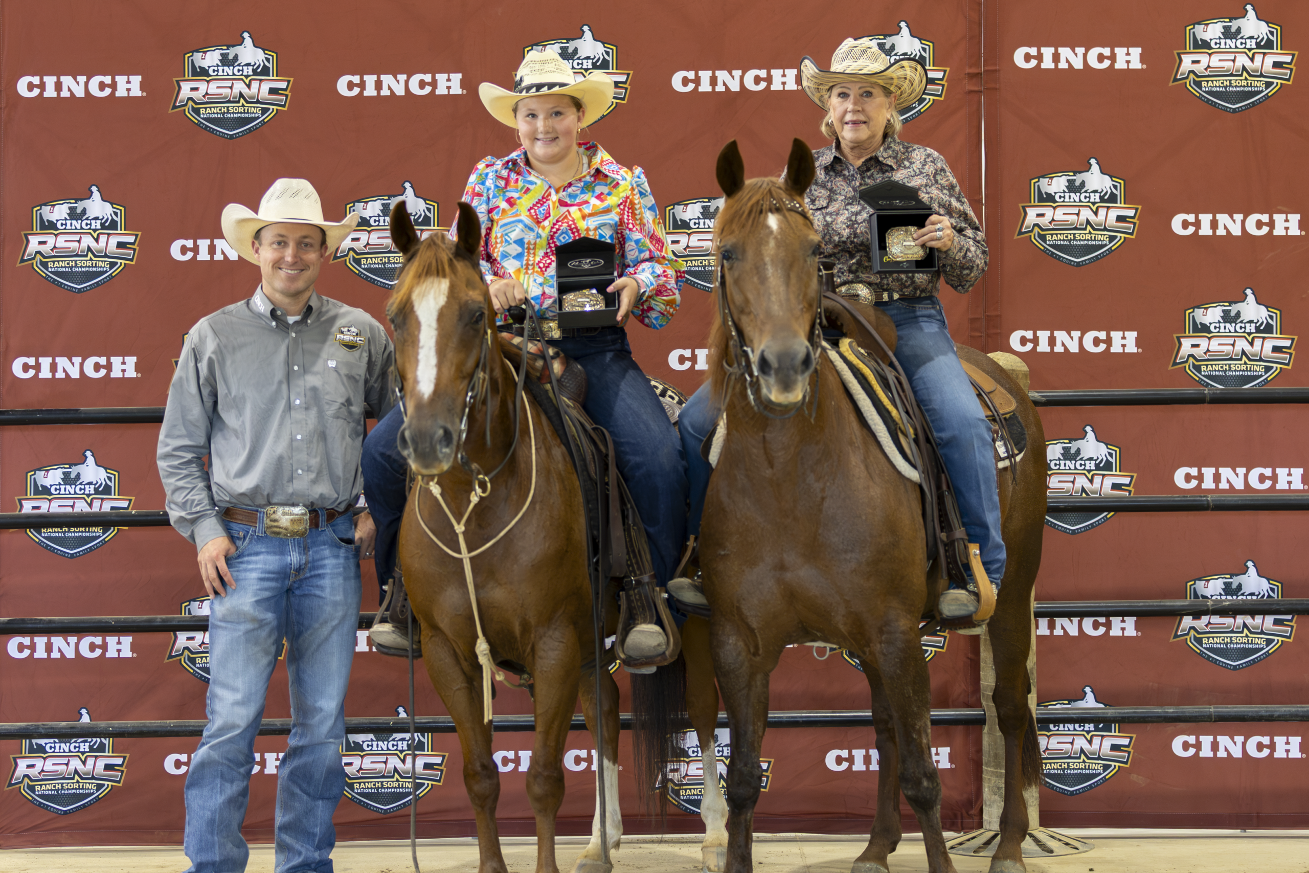 Three mounted cowboys and a handler pose with horses at a Cinch-branded rodeo backdrop