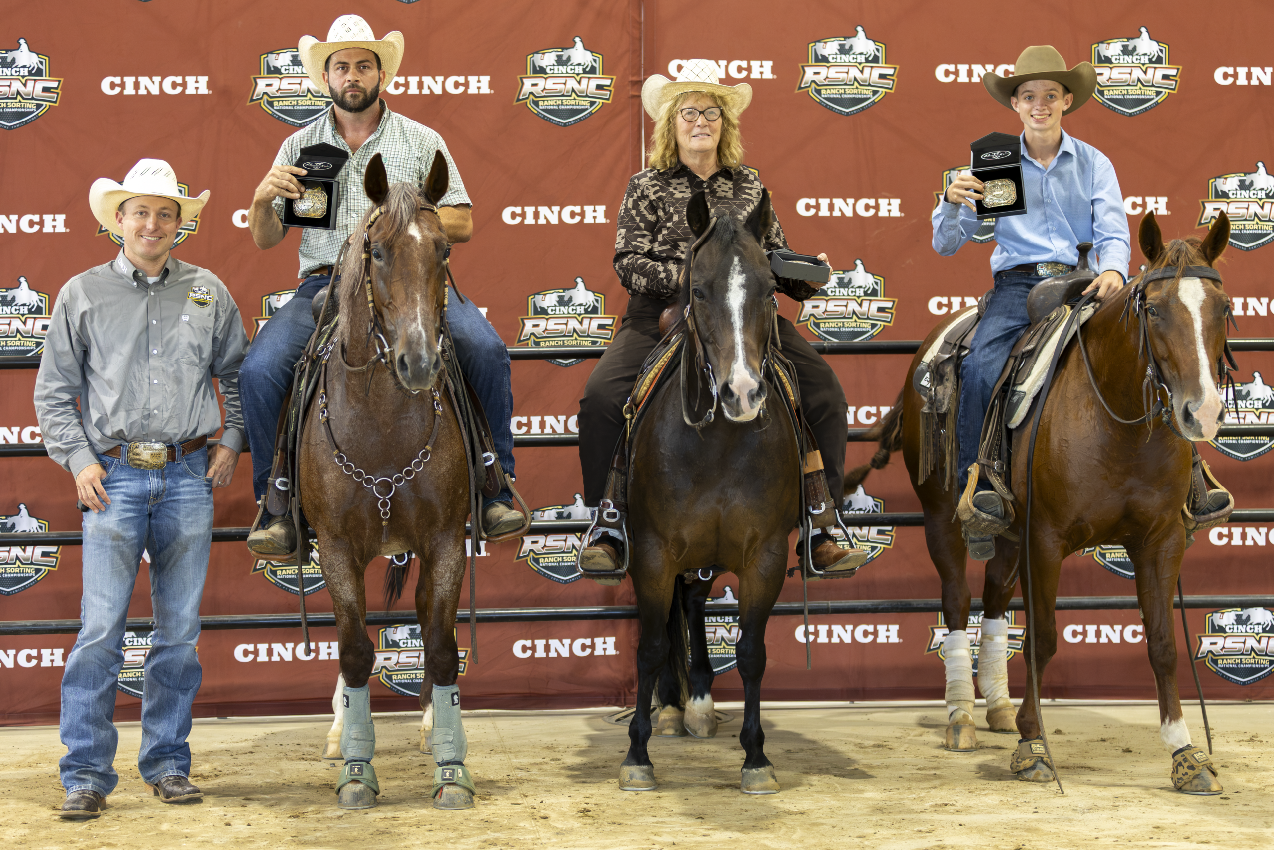 Four cowboys and cowgirls stand with their horses at a Cinch-branded backdrop after a rodeo event competition