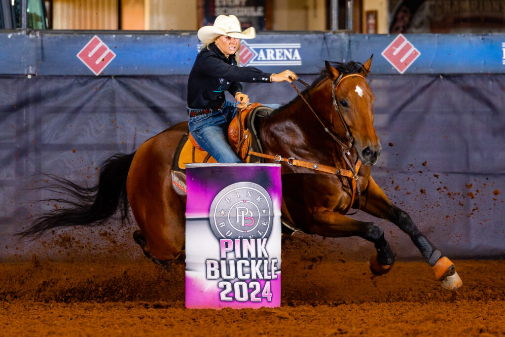 Barrel racer in a black shirt and cowboy hat turns her bay horse tight around a Pink Buckle 2024 barrel