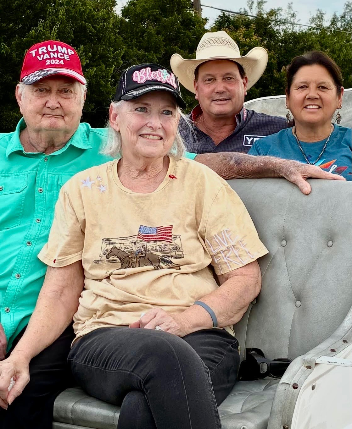 Four people pose together in a vehicle at what appears to be a rodeo or western event, with one holding a large catfish