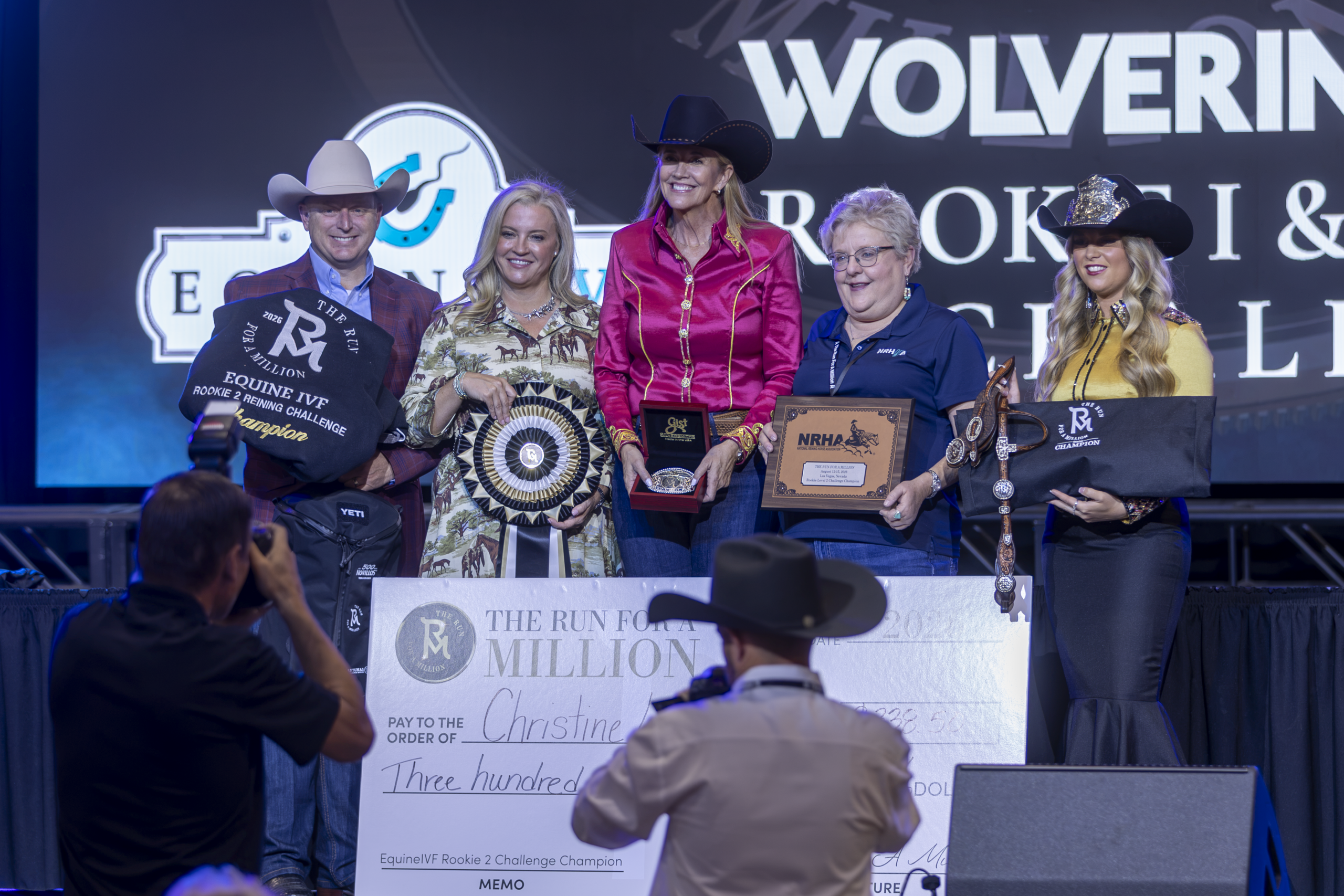 Winners and officials pose on stage with awards and a large check at a Wolverine rodeo event