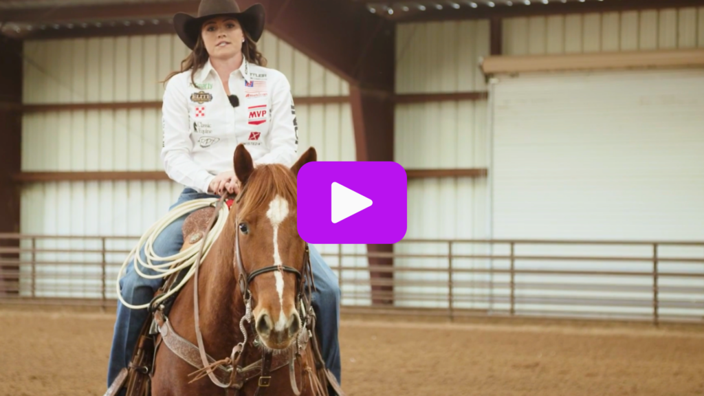 Cowgirl in a black hat and sponsor-patched white shirt rides a sorrel horse with a coiled rope in a covered arena