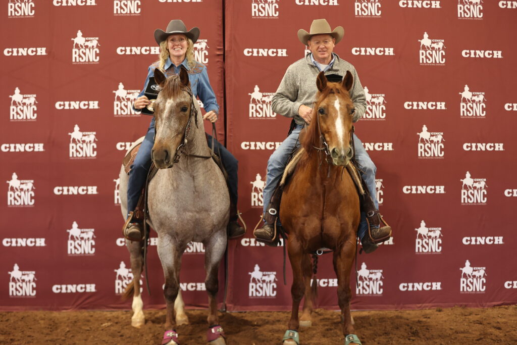 Two riders in cowboy hats sit horseback, one holding a trophy, in front of a Cinch RSNC backdrop