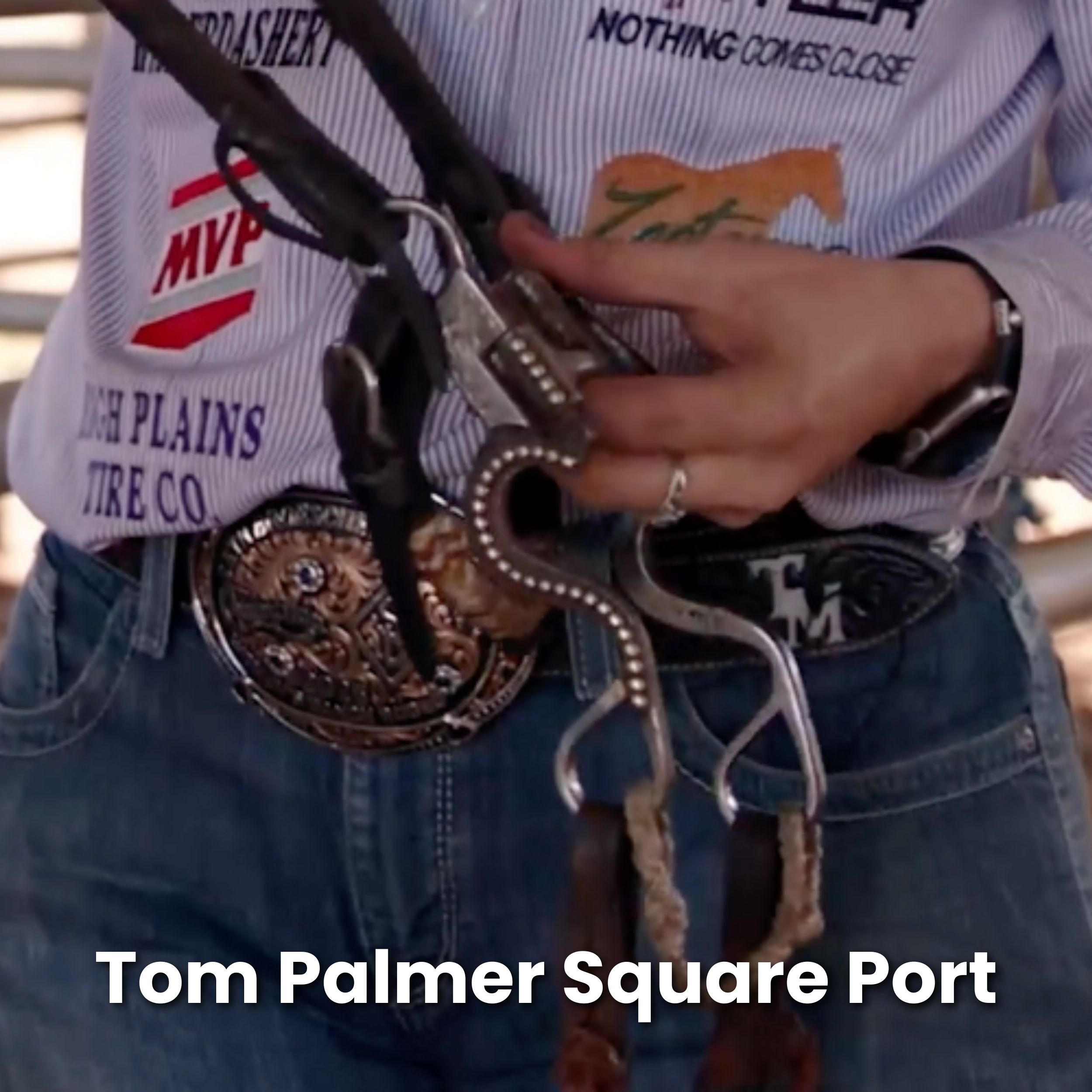 Close-up of a cowboy in a sponsor-patched shirt holding a silver-mounted bit with a square port mouthpiece, worn belt buckles at his waist