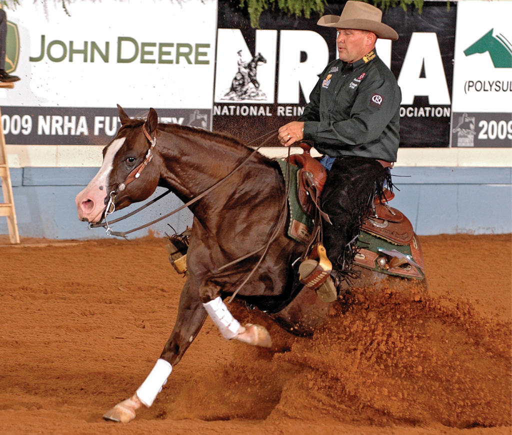 Reiner in a cowboy hat slides his sorrel horse to a dramatic stop, kicking up dirt in front of NRHA Futurity banners